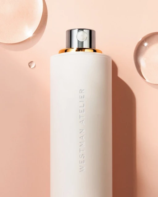 Close-up of a white cosmetic bottle with silver accents and the words WESTMAN ATELIER, set against a light peach background.