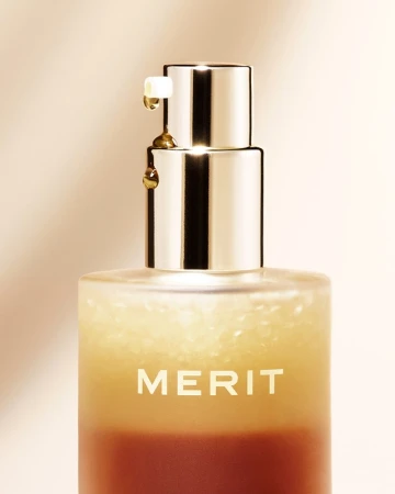 Close-up of a bottle of Merit beauty serum with a pump dispenser and golden liquid dripping from the nozzle, set against a beige background.