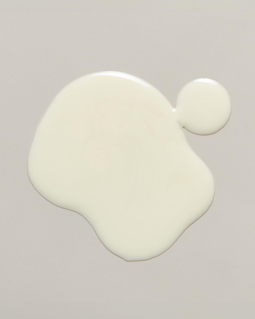 Overhead shot of a blob of spilled white fluid on a gray surface. The white fluid has an organic, irregular shape.