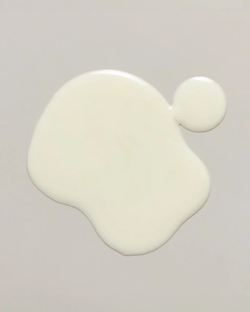 Overhead shot of a blob of spilled white fluid on a gray surface. The white fluid has an organic, irregular shape.
