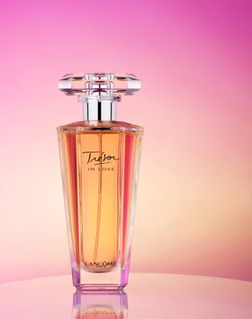 Elegant still life of a 'Tresor in Love' perfume bottle by Lancome, featuring a clear, faceted cap and a gradient pink and peach background.