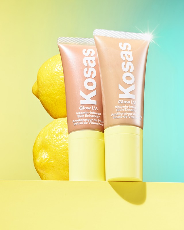 Two Kosas Glow IV skin enhancer tubes with lemons against a split yellow and blue background, showcasing beauty and skincare.