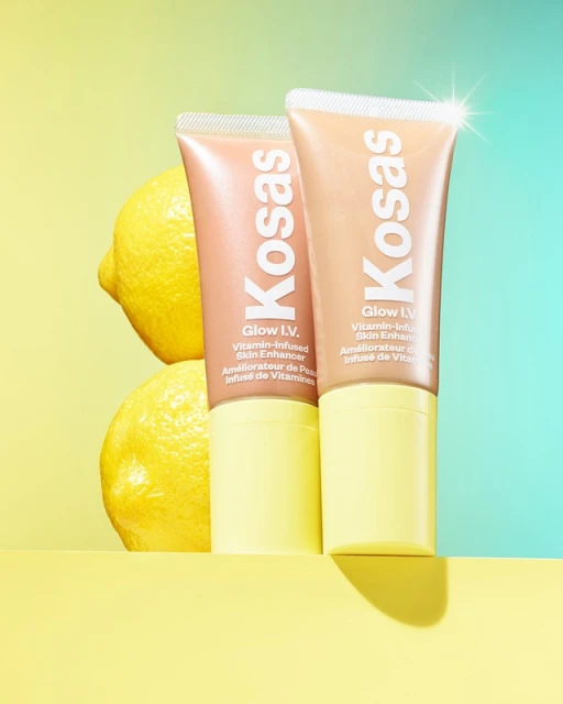 Two Kosas Glow IV skin enhancer tubes with lemons against a split yellow and blue background, showcasing beauty and skincare.
