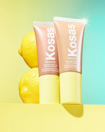 Two Kosas Glow IV skin enhancer tubes with lemons against a split yellow and blue background, showcasing beauty and skincare.
