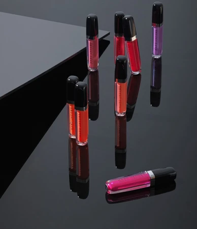 Multiple lip gloss tubes standing upright and lying on a dark reflective surface