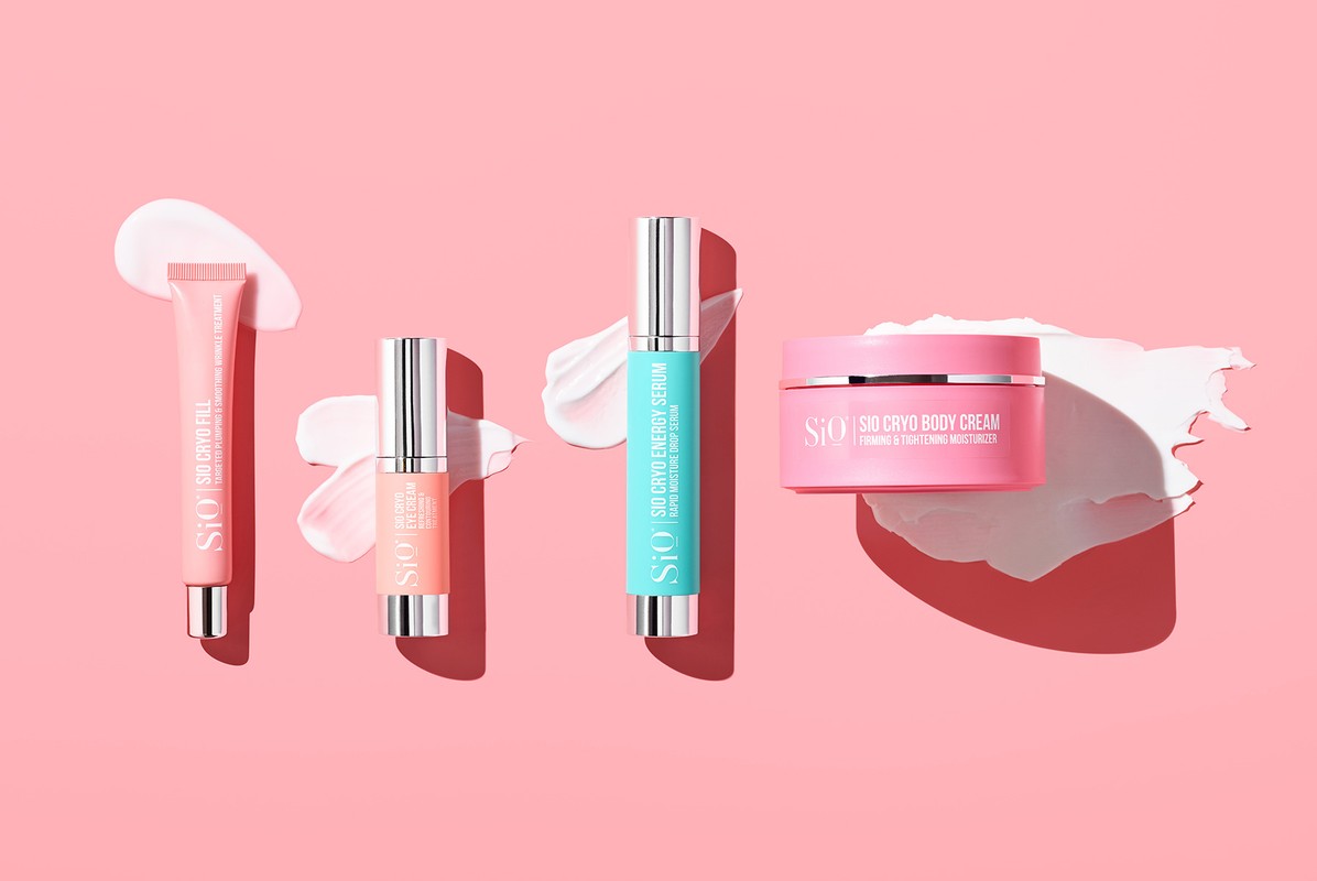 Arrangement of Sio Cryo skincare products: Fill, Eye Cream, Energy Serum, and Body Cream on a pink background with cream smears.