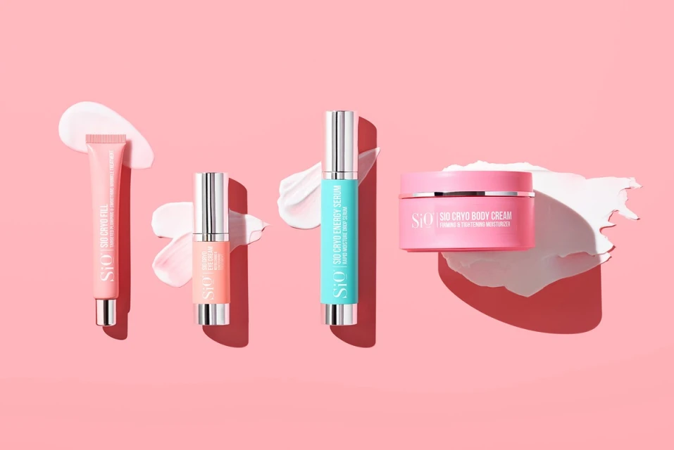 Arrangement of Sio Cryo skincare products: Fill, Eye Cream, Energy Serum, and Body Cream on a pink background with cream smears.