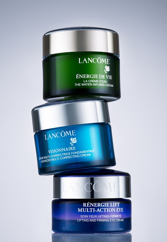 Three Lancôme skincare product jars stacked. The jars are green, blue, and dark blue with silver lids and product branding visible.