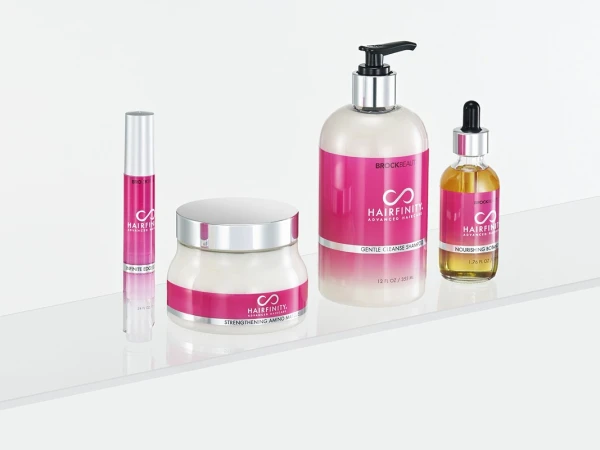 Hairfinity haircare product line on a white surface includes shampoo, oil, mask, and serum, featuring pink labels with the Hairfinity logo.