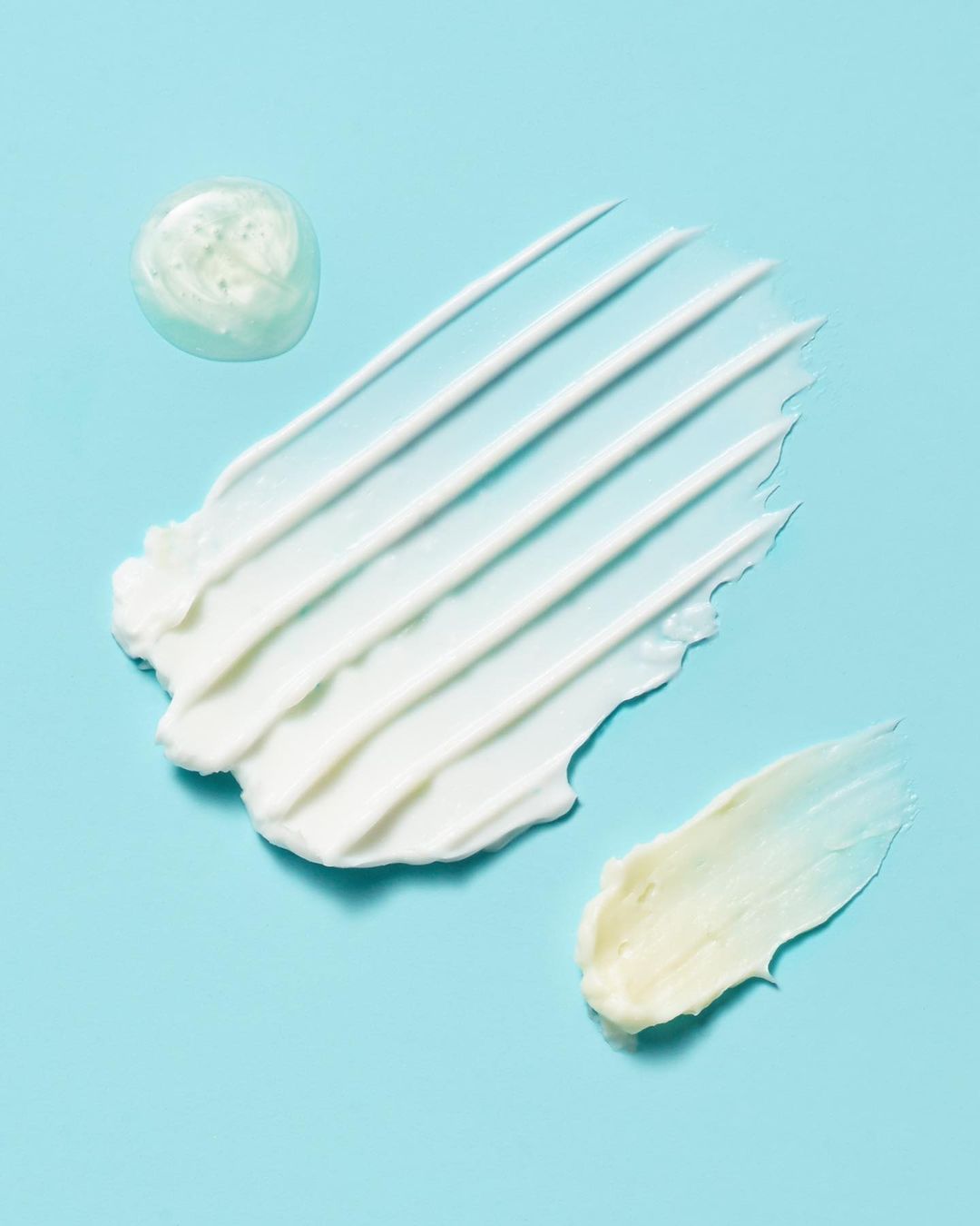 Close-up shot of white and clear skincare product smears against a light blue backdrop. Ideal for beauty and cosmetic promotions.