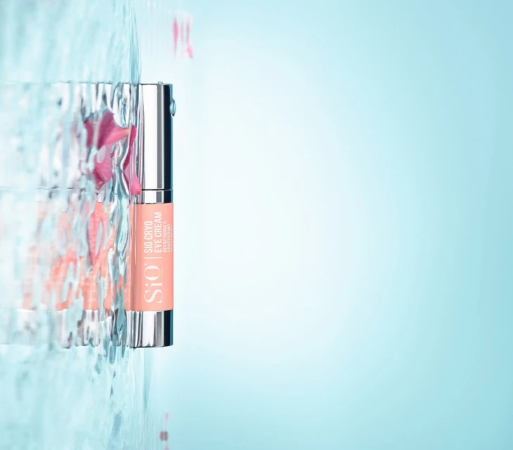 Sio Cryo eye cream product shot with water and flower petals. The eye cream tube is salmon-colored with silver accents.