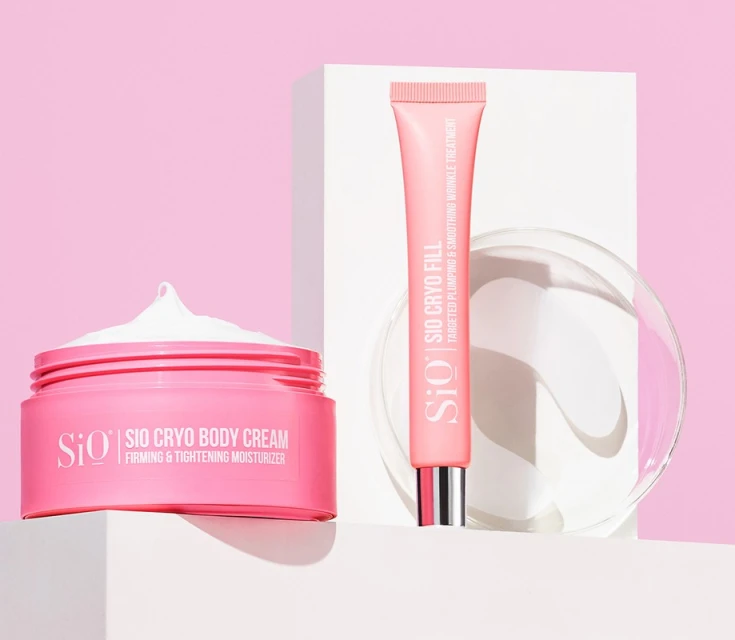 Close-up of Si0 Cryo Body Cream jar and Cryo Fill tube against pink and white background, showcasing beauty and skincare products.