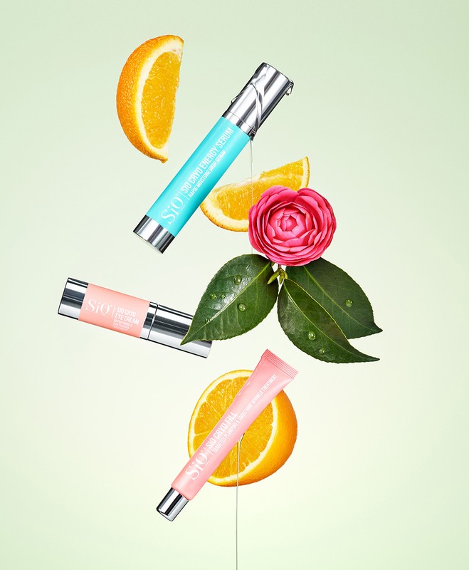Cosmetic products from skincare and beauty brands floating with orange slices and pink flower on light green background in studio shot.