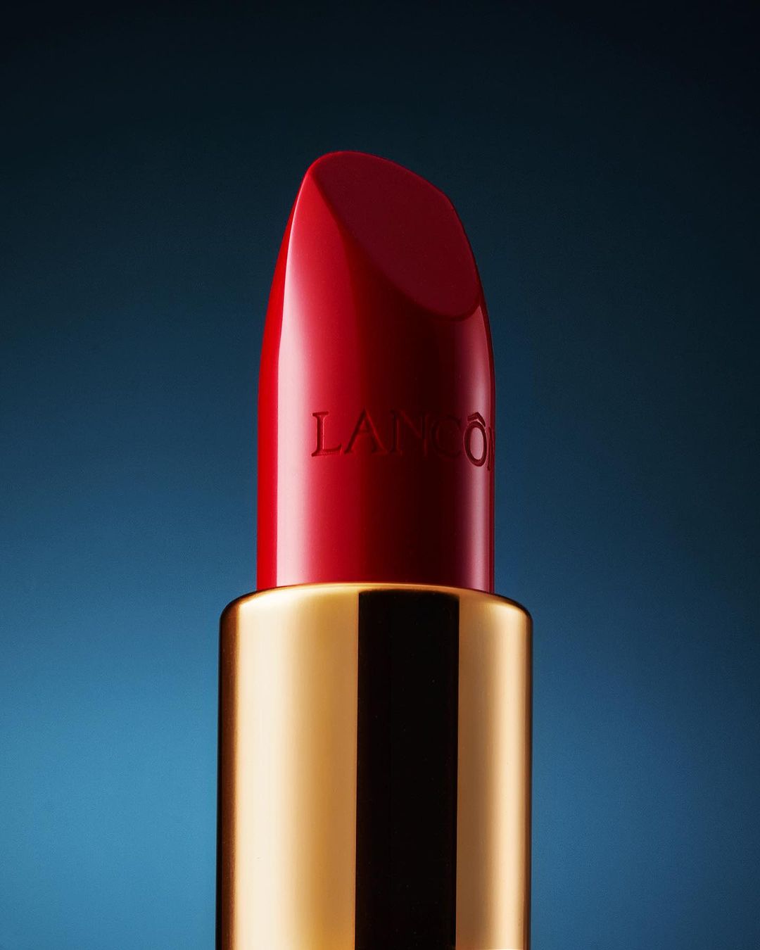 Close-up of a red Lancôme lipstick with a gold tube against a smooth blue gradient backdrop, emphasizing luxury beauty.