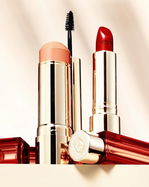 Cosmetic product photo: a lipstick, brow gel, and blush stick arranged closely together in a studio setting with soft lighting.