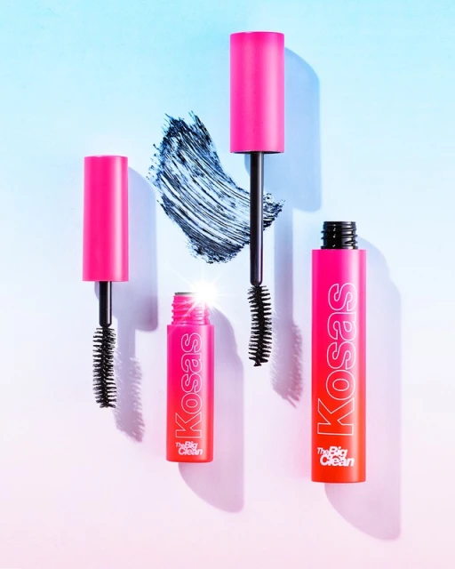 Four pink and orange Kosas mascara tubes and applicators, surrounded by a light blue and white gradient background, with brush strokes.