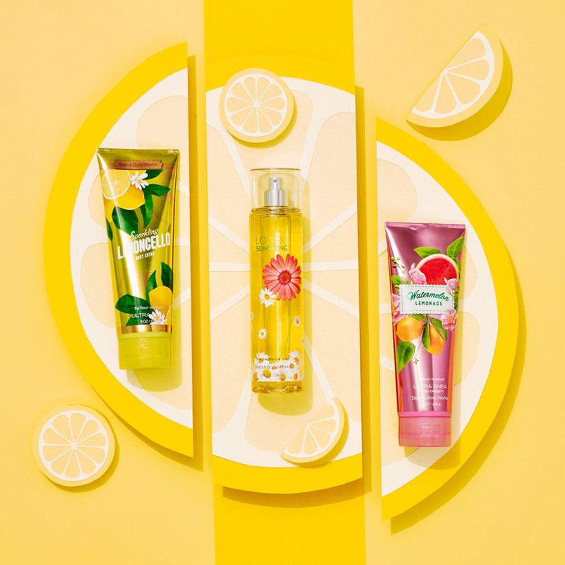 Three cosmetic product tubes and a spray bottle arranged with lemon slices on a bright yellow background in a studio shot.