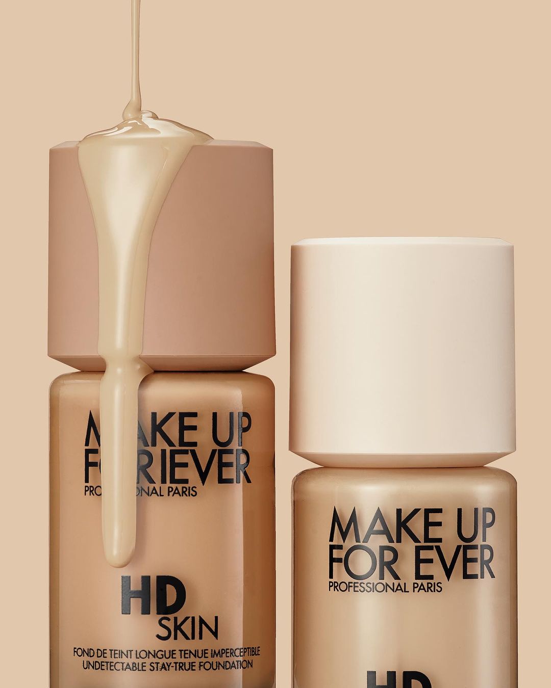 Cosmetic still life: Makeup Forever HD Skin foundation bottles are displayed with foundation liquid dripping over one of the bottles.