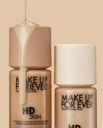 Cosmetic still life: Makeup Forever HD Skin foundation bottles are displayed with foundation liquid dripping over one of the bottles.