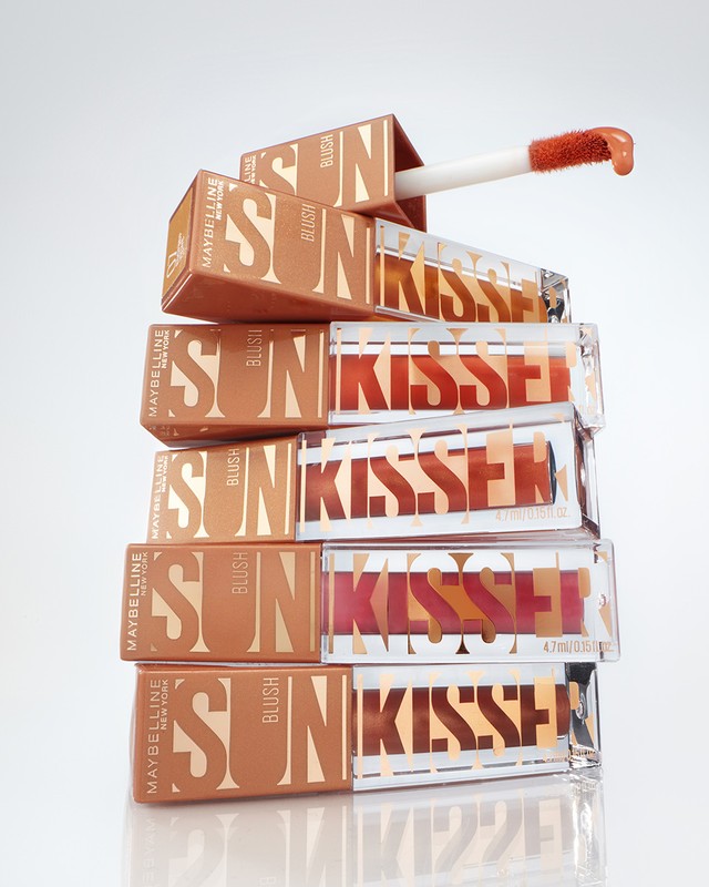 A stack of Maybelline Sun Kissers lip gloss products in their packaging on a clean white surface, capturing a beauty product shot.