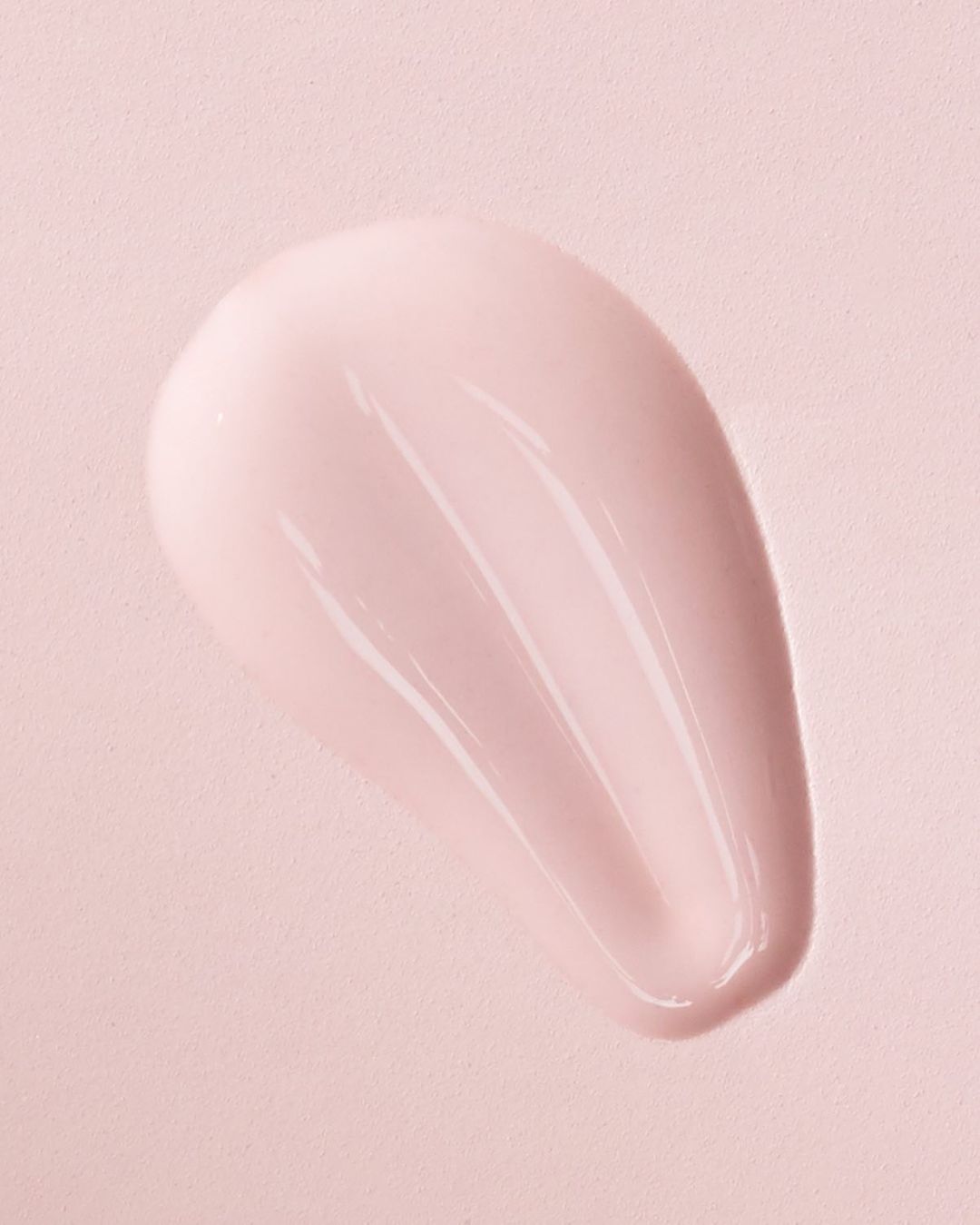 Close-up of a pink cosmetic cream swatch smeared on a matching pink textured background surface.