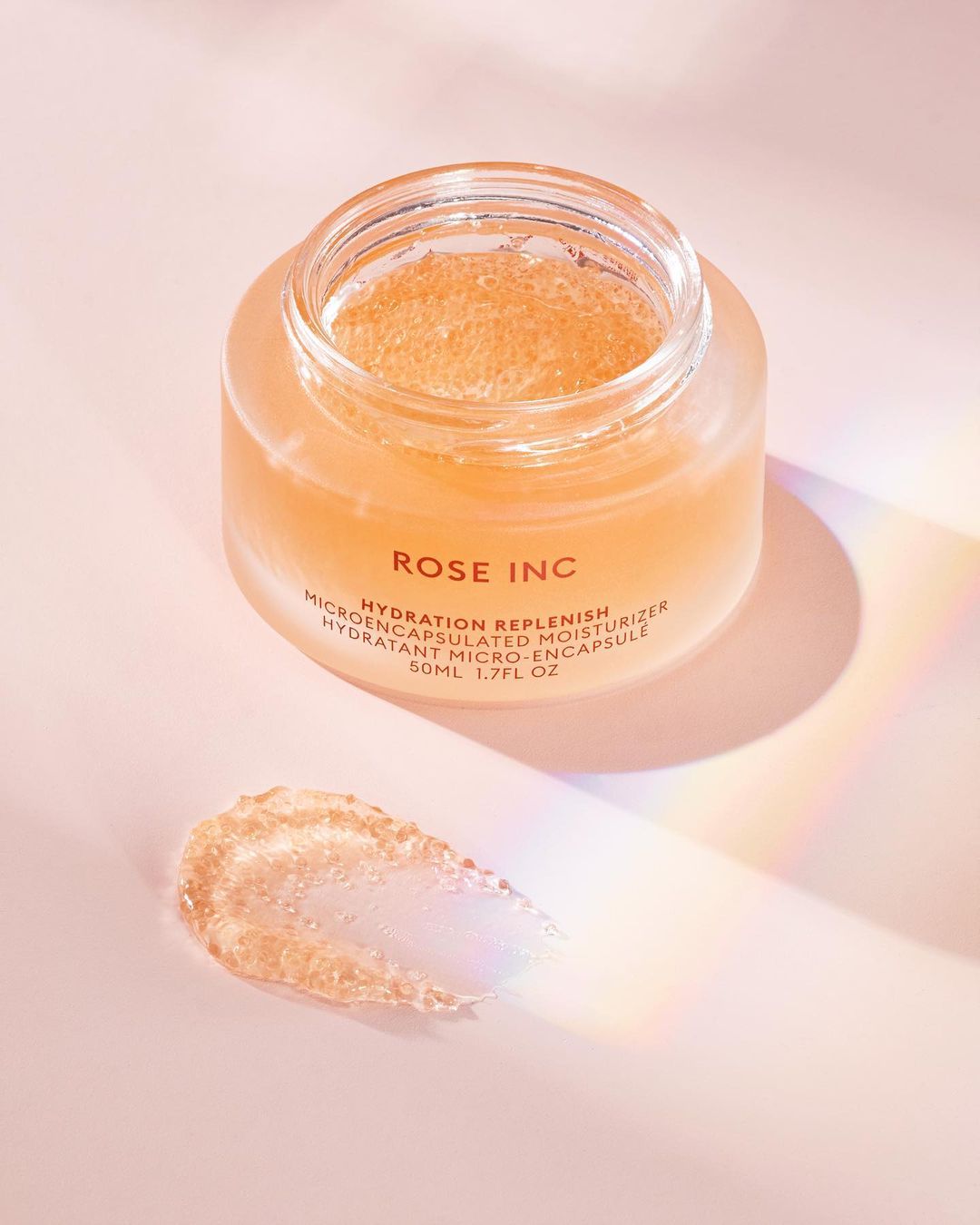 Rose Inc Hydration Replenish moisturizer in a glass jar with product swatch on a pink surface with light and shadow effects.