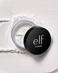Top down product shot of an elf HD powder jar resting on a textured white surface surrounded by loose white cosmetic powder