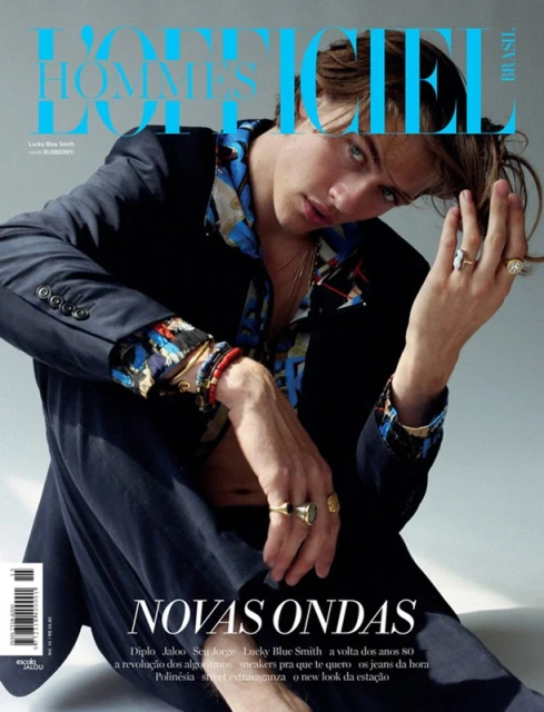 Magazine cover of a male fashion model, Lucky Blue Smith, posing in a navy suit jacket, patterned shirt, and multiple rings.