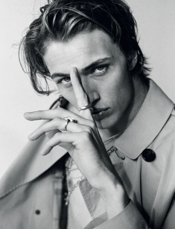 Close up monochrome portrait of a young man with rings on his fingers wearing a light coat styled by Marc Anthony George