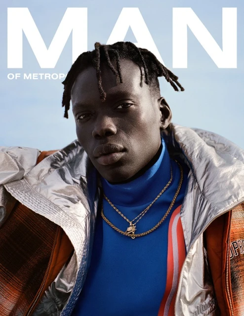 Magazine cover featuring a stylish Black man with dreadlocks wearing designer clothing and gold necklaces against a blurred background.
