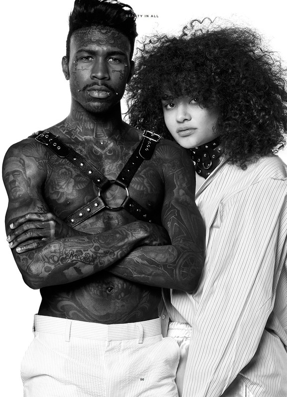 Monochrome studio portrait of a heavily tattooed, bare-chested Black male model with a White female model sporting an afro.