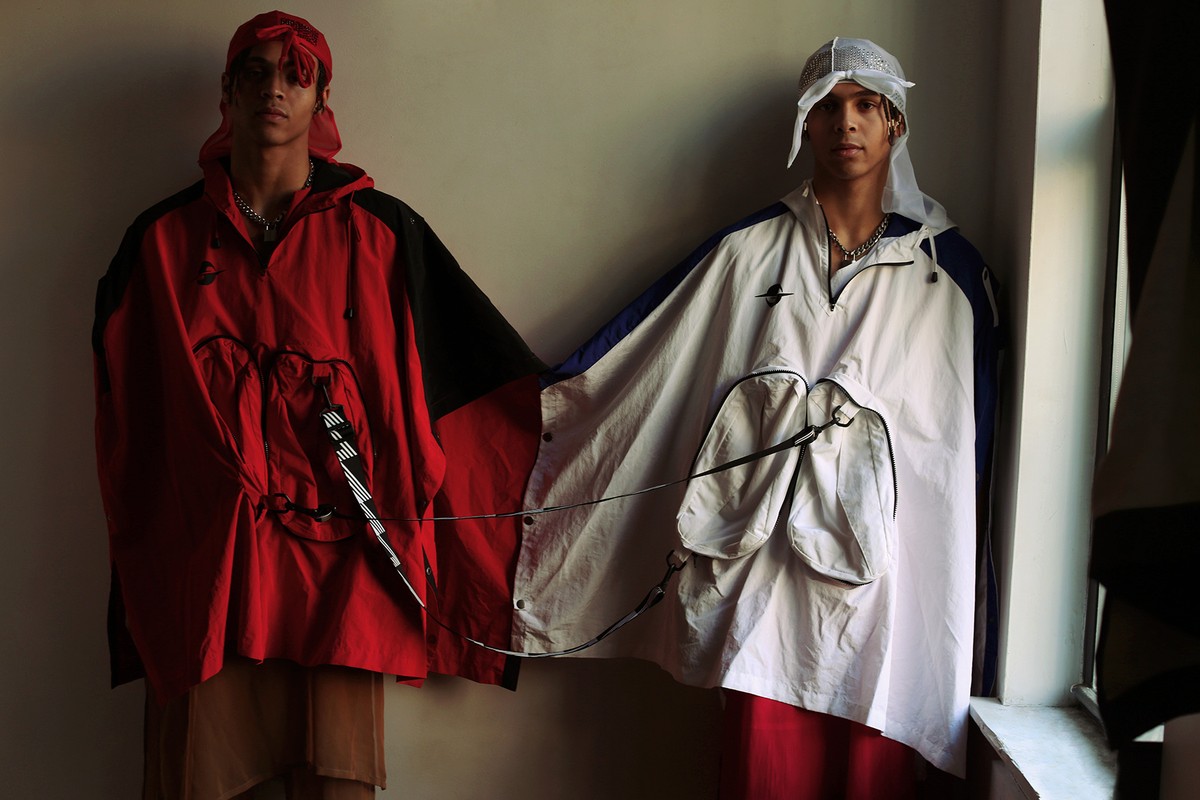 Two young men in fashionable oversize hooded jackets pose indoors wearing headscarves, showcasing streetwear fashion and modern design.