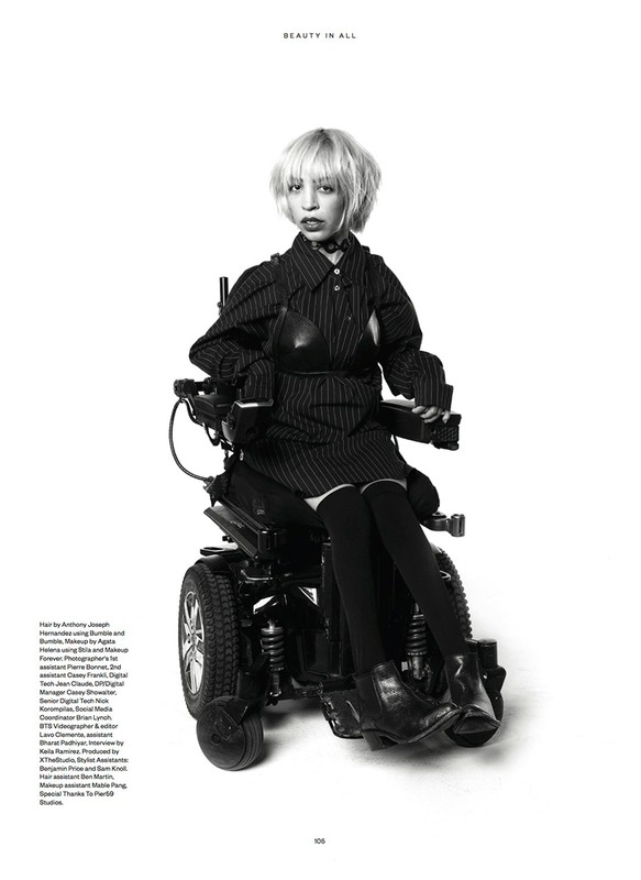 Monochrome fashion shot of a woman in a pinstripe outfit sitting in a powered wheelchair against a clean white backdrop.