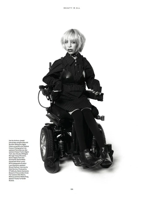 Monochrome fashion shot of a woman in a pinstripe outfit sitting in a powered wheelchair against a clean white backdrop.