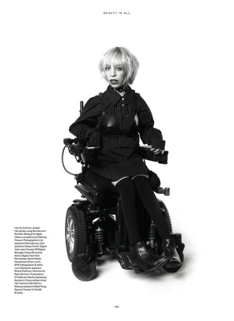 Monochrome fashion shot of a woman in a pinstripe outfit sitting in a powered wheelchair against a clean white backdrop.