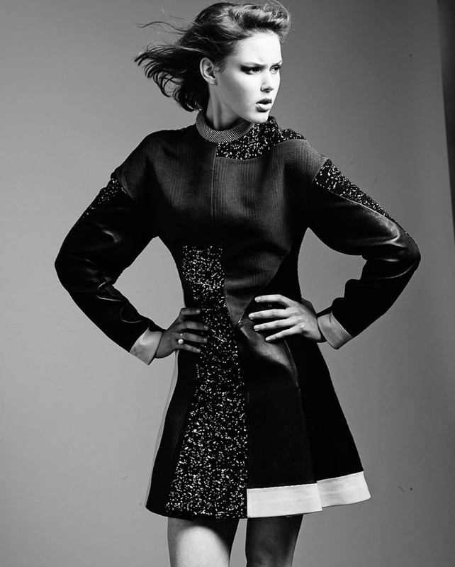 Black and white portrait of an adult woman posing in a short, patterned dress in a photo studio with a neutral background.