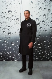 Man wearing a black coat standing against a backdrop patterned with water drops