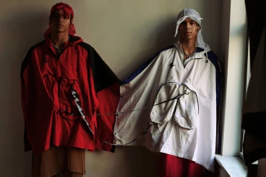Two men standing side by side wearing oversized utility ponchos and headscarves styled by Marc Anthony George in Los Angeles