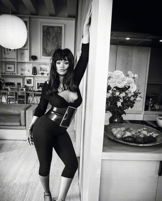 Black and white portrait of a woman in a sleek black outfit posing in an indoor setting, with an emphasis on the outfit and setting.