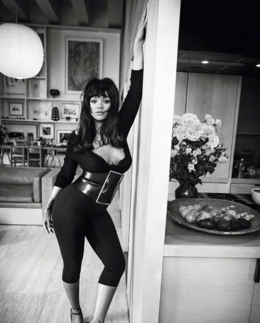 Black and white portrait of a woman in a sleek black outfit posing in an indoor setting, with an emphasis on the outfit and setting.
