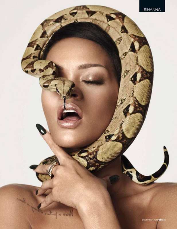 Portrait of a topless adult female with closed eyes, posing with a snake wrapped around her head and neck in a bright indoor setting.