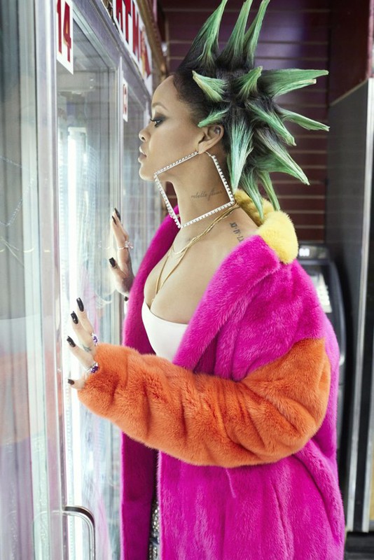 Woman with green mohawk and colorful fur coat looks at display case indoors, wearing large square earrings and multiple rings.