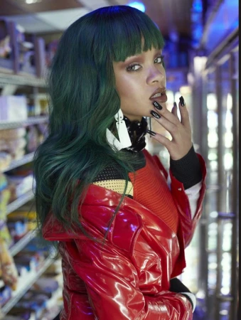 A woman with green hair, red coat, and black nails poses in front of shelves with grocery items in an indoor setting.