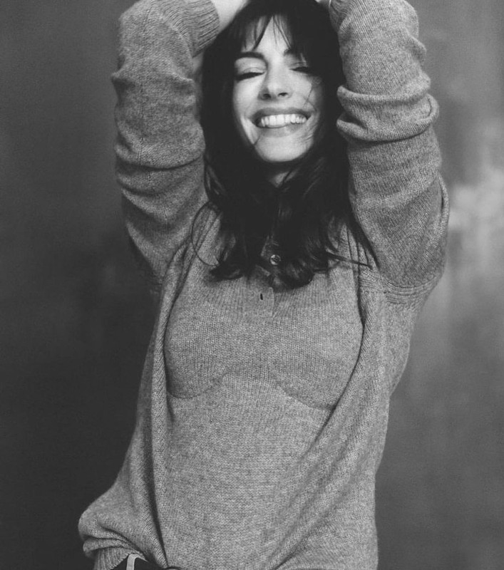 Black and white portrait of a woman with dark hair smiling and looking up while wearing a gray sweater against a neutral backdrop.