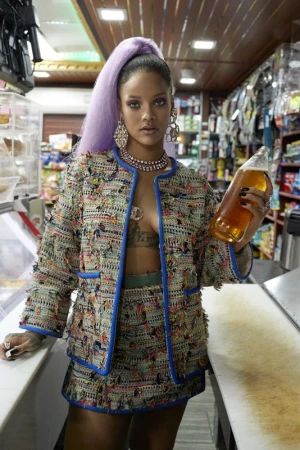 Stylish adult woman in a tweed skirt suit holds a large bottle inside a bodega setting, complete with shelves and overhead storage.