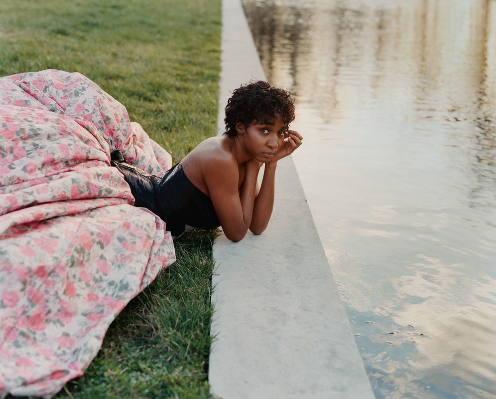 Woman laying by a pool, draped with a floral blanket, resting her chin on her hands in natural light, capturing a serene outdoor moment.