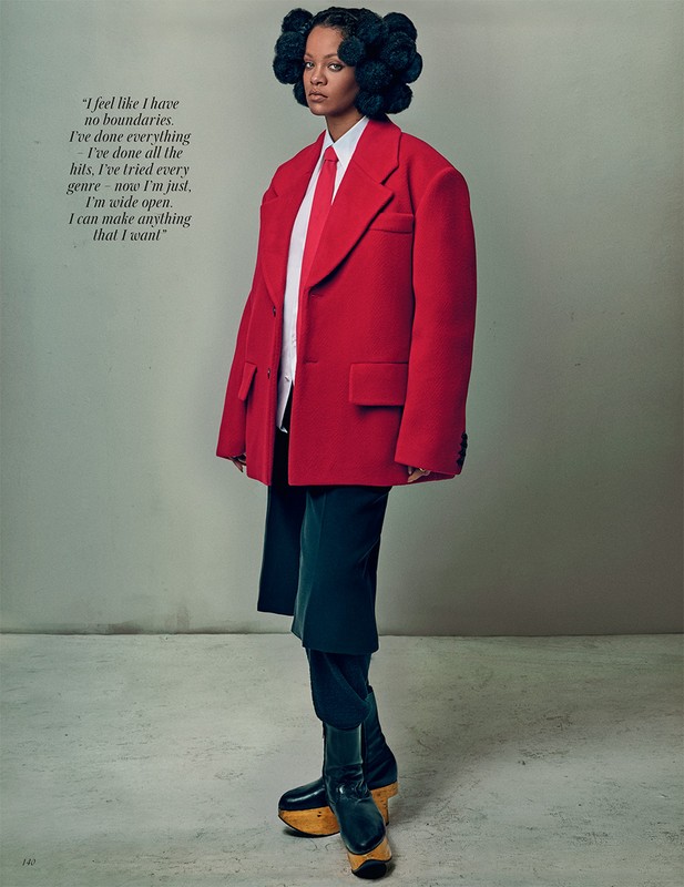 Stylish woman in oversized red blazer, white shirt, and platform shoes strikes a pose in a fashion editorial-style portrait on grey.