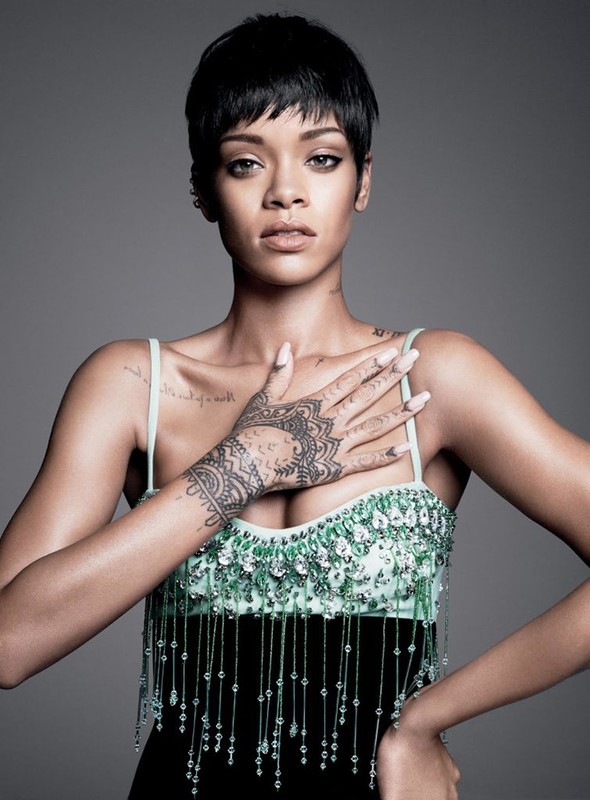 Close-up portrait of Rihanna with short dark hair, wearing a beaded black and teal dress, against a gray background in a photo studio.