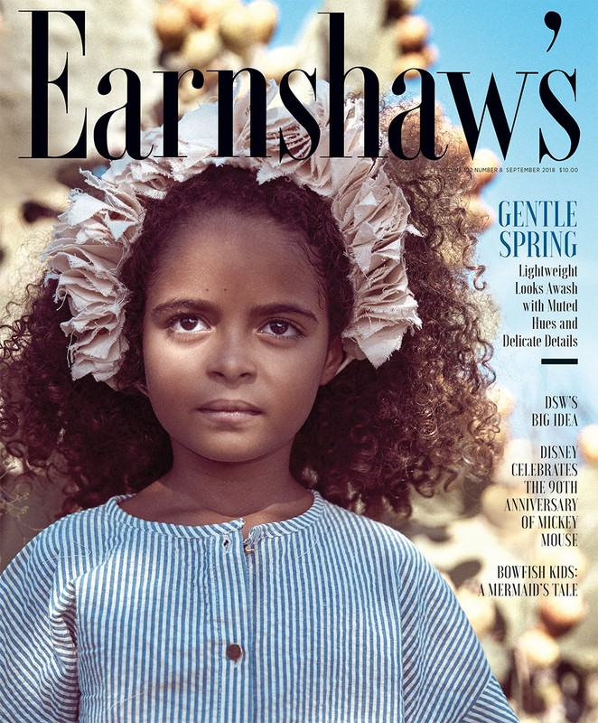 Magazine cover featuring a young girl with curly hair and a floral headpiece, wearing a blue and white striped dress, against a blurred outdoor background.