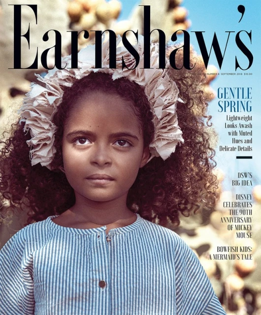 Magazine cover featuring a young girl with curly hair and a floral headpiece, wearing a blue and white striped dress, against a blurred outdoor background.